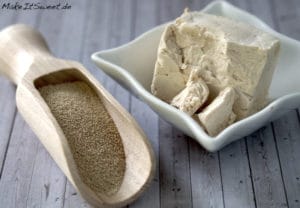 Trockenhefe in einer Holzkelle und frische Hefe in einer Schüssel auf einer Holzunterlage.