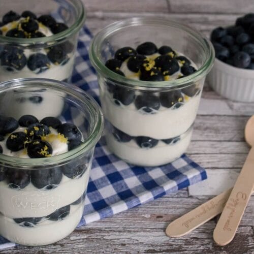 Drei Gläser Quark mit Blaubeeren, die mit weiteren Blaubeeren belegt sind.