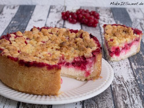 Ein Stück Johannisbeerkuchen mit Quark und Streusel auf einem Teller mit roten Johannisbeeren.