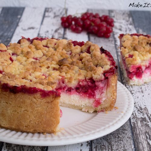 Ein Stück Johannisbeerkuchen mit Quark und Streusel auf einem Teller mit roten Johannisbeeren.