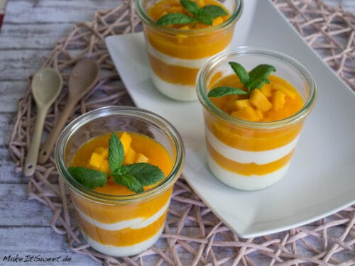 Drei Gläser mit geschichtetem Mango-Quark-Dessert, garniert mit frischen Mangostücken, auf einem weißen Teller.