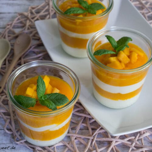 Drei Gläser mit geschichtetem Mango-Quark-Dessert, garniert mit frischen Mangostücken, auf einem weißen Teller.