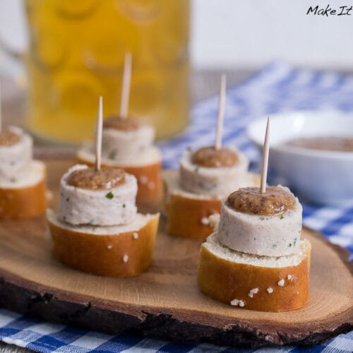 Fünf Wurstwurst- und Brezeläppchen mit Zahnstochern auf einem Holzbrett.