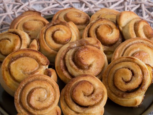 Goldbraune Mini-Zimtschnecken mit Zimt und Zucker, angerichtet auf einem dunklen Teller.