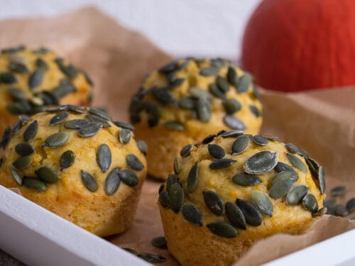 Süße Kürbismuffins mit Zimt in einem Tablett, mit einem Kürbis im Hintergrund.