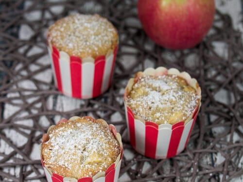 Apfelmuffins in rot-weißen Bechern, bestäubt mit Puderzucker.