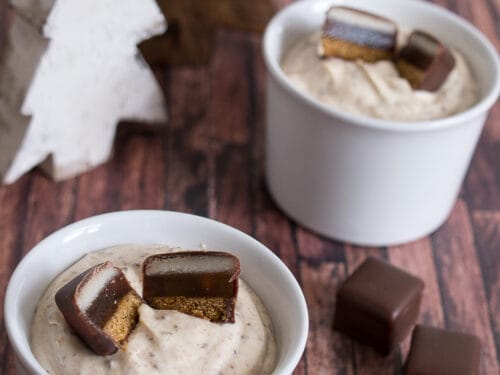 Zwei Becher mit cremigem Dominostein-Dessert, jeweils mit schokoladenüberzogenen Leckereien bestückt.