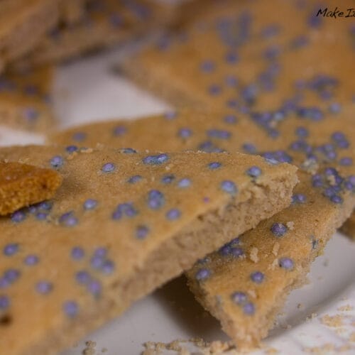 Flache beige Schokoladen-Ingwer-Plätzchen mit Zuckerstreuseln auf einem weißen Teller.
