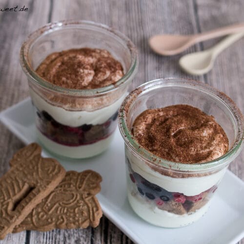 Spekulatius-Beeren-Tiramisu 3 Geschichtetes Dessert aus einer Creme, Beeren und Kakaopulver in zwei Gläsern mit je einem Spekulatius auf einem weißen Teller.