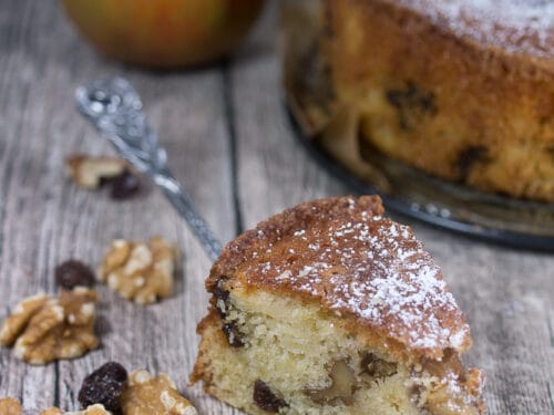 Apfel-Walnuss-Kuchen Stück mit Rosinen auf einer Gabel, mit Walnüssen, Rosinen und einem Apfel in der Nähe.