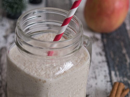 Smoothie mit Apfel und Zimt in einem Einmachglas mit rotgestreiftem Strohhalm, Apfelscheiben und Zimtstangen.