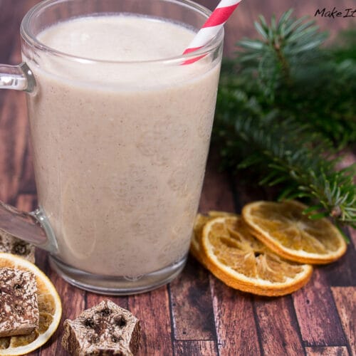Glasbecher mit cremigem Orangen-Smoothie mit Lebkuchen und rot gestreiftem Strohhalm.