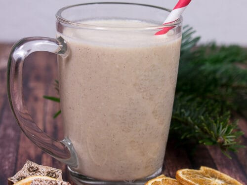 Ein Glas cremiger Orangen-Lebkuchen-Smoothie mit einem rot-weißen Strohhalm.