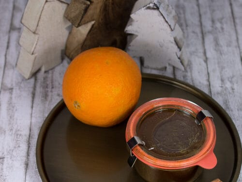 Eine Orange, ein Glas Marmelade mit Orange und Spekulius und eine Zimtstange auf einem Tablett.
