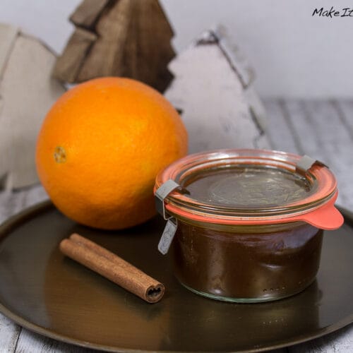 Marmelade mit Orange und Spekultius 3 Ein Glas Marmelade mit Orange und Spekultius, eine Orange und eine Zimtstange auf einem runden Tablett.