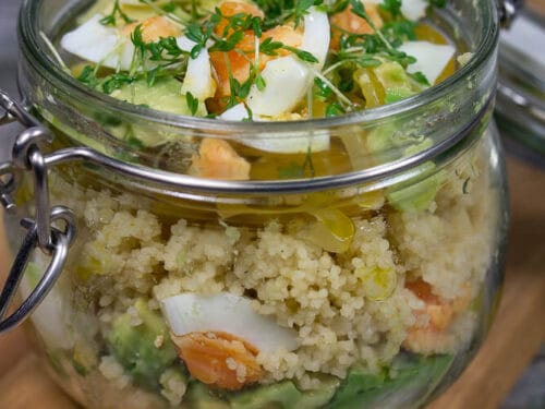 Ein Glas mit Couscous-Salat mit Avocado, gekochtem Ei und frischer Kresse auf einem Holzbrett.