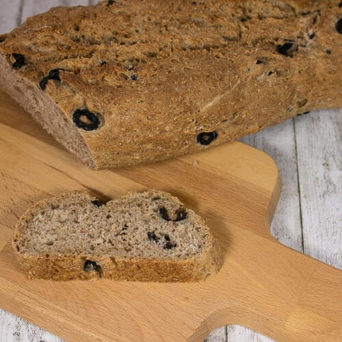 Vollkornbrot mit Olivenbrot und einem aufgeschnittenen Stück auf einem hölzernen Schneidebrett.