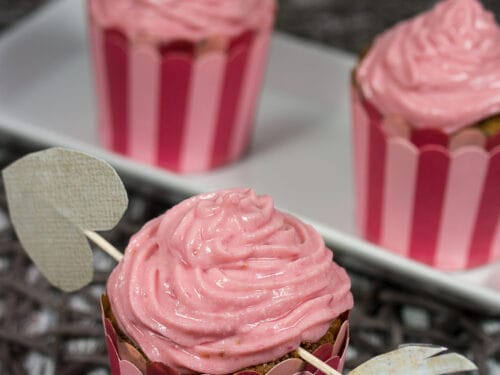 Drei Himbeere-Muffins mit Himbeeren-Topping in rot-gestreiften Verpackungen auf einem Tablett.