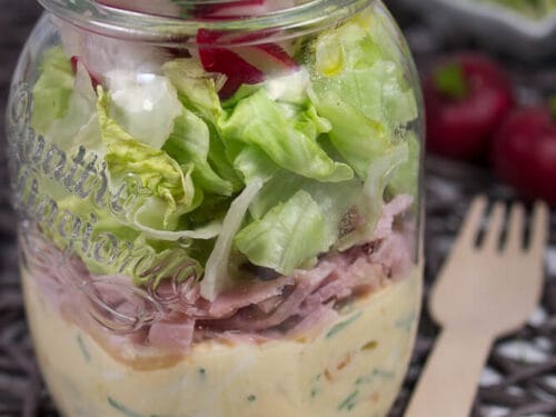 Salat im Glas mit Schichten aus grünem Salat, Schinken, Radieschen und Sauce, serviert im Mason Jar.