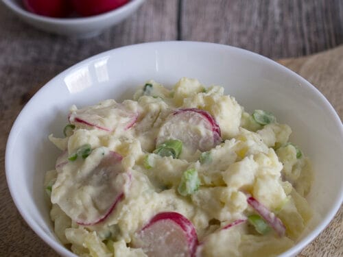 Kartoffelsalat mit geschnittenen Radieschen und Frühlingszwiebeln auf einem Teller.