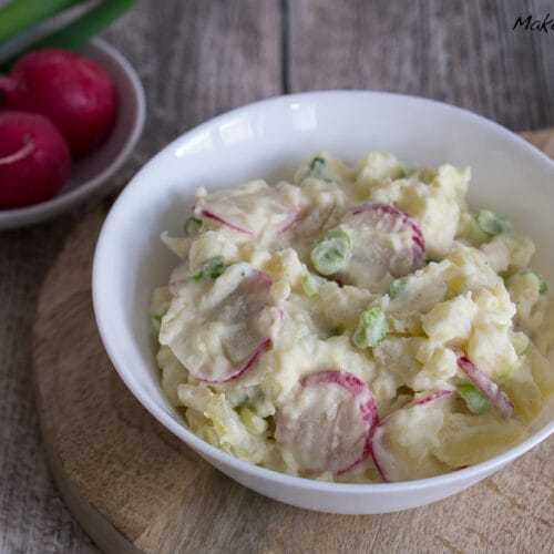 Kartoffelsalat mit Radieschen 3 Kartoffelsalat mit geschnittenen Radieschen und Frühlingszwiebeln in einer Schüssel, daneben ganze Radieschen.