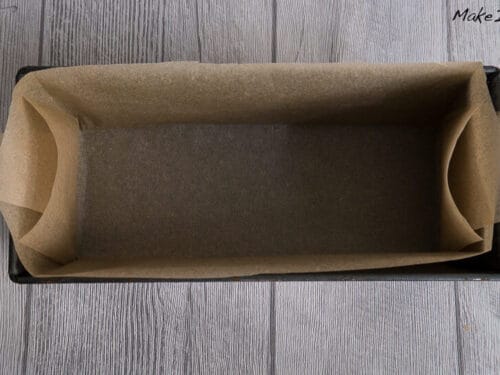 Eine mit gefaltetem Backpapier ausgelegte Kastenform, bereit zum Backen.
