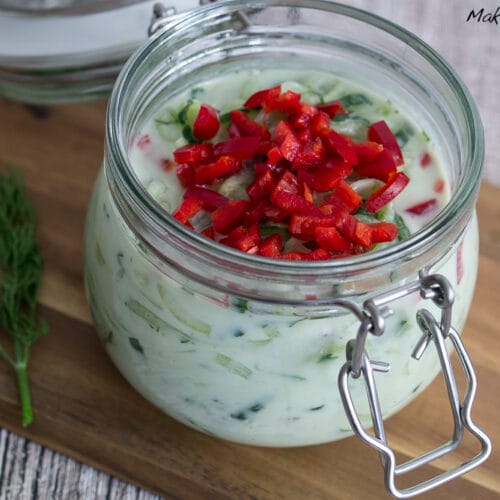 Glas mit cremigem Gurken Salat mit Joghurt, belegt mit gewürfelter roter Chili und frischem Dill.