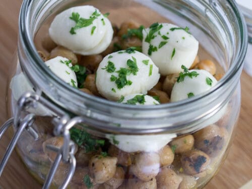 Salat im Glas gefüllt mit Kichererbsensalat, Mini-Tomaten, Mozzarellakugeln, gehackten Kräutern und Dressing.
