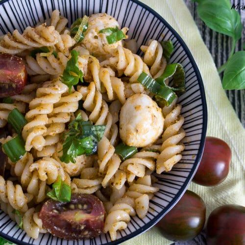 Pesto Nudelsalat mit Mozzarella und Tomate 3 Pesto Nudelsalat mit Mozzarella, Tomaten und Basilikum, serviert in einer Schüssel auf einem gestreiften Teller.
