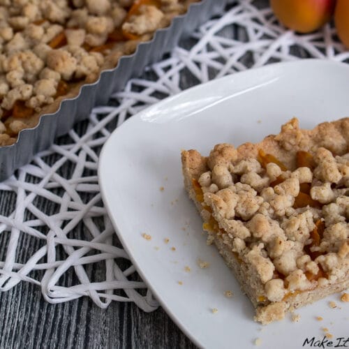 Aprikosen Tarte mit Streuseln und Zimt 3 Ein Stück Aprikosen-Tarte mit Streuseln auf einem Teller neben einer gefüllten Backform.