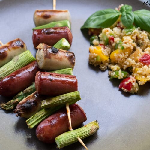 Praktisch zum Grillen: Bratwurstspieße 3 Bratwurst-Spargel-Spieße vom Grill mit Quinoa-Salat und frischem Basilikum auf einem Teller.