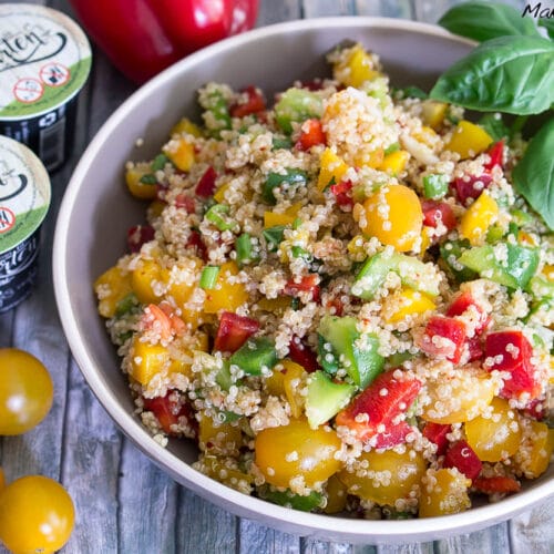 Schüssel mit Quinoa-Salat mit gelben Tomaten, Avocadoscheiben, roter Paprika und Basilikum.