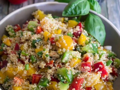Schüssel mit Quinoa-Salat mit gelben Tomaten, roter Paprika, Avocado und Basilikum.
