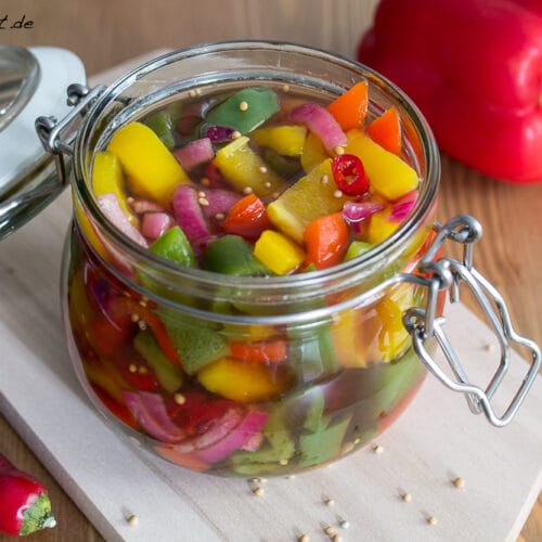Eingelegtes Gemüse im Glas mit Paprika-Antipasti und roten Paprikaschoten auf einem Holzbrett.