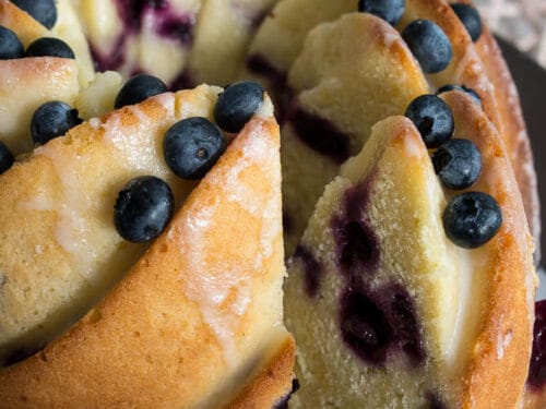In Scheiben geschnittener Gugelhupf mit Heidelbeeren und Zitronen-Glasur auf einem braunen Teller.
