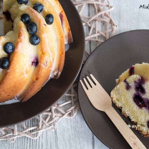 Gugelhupf mit Blaubeeren, Zitronen und Buttermilch 3 Gugelhupf mit Blaubeeren auf einem braunen Teller, mit einer Scheibe auf einem kleineren Teller und einer Holzgabel.