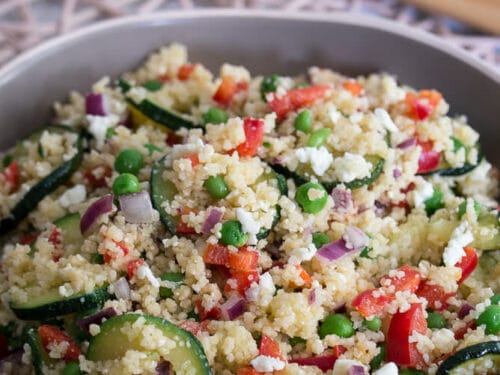Schüssel mit Couscous-Salat mit Zucchini, Erbsen, roter Paprika, Zwiebeln und Fetakäse.