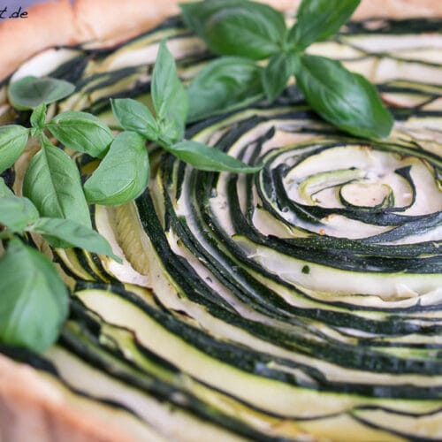 Zucchini Tarte mit Basilikum 3 Zucchini-Tarte mit spiralförmigen Zucchini auf einer goldenen Kruste. Frische Basilikumblätter als Garnitur.