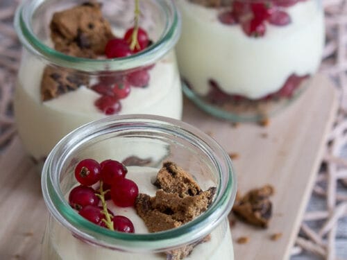 Drei Gläser mit cremigem Johannisbeer-Dessert mit Mango, gekrönt mit roten Johannisbeeren und zerbröselten Cookies.
