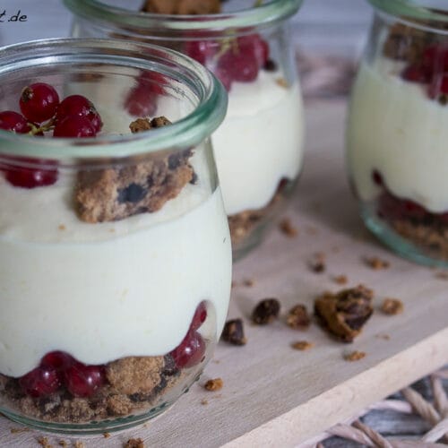Johannisbeer-Dessert mit Mangocreme und Cookies im Glas 3 Drei Gläser mit Schichten aus Mangoquark, roten Johannisbeeren und zerbröselten Cookies.