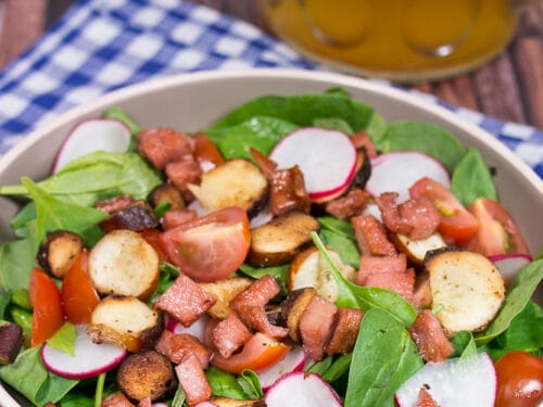 Frischer Oktoberfest-Salat mit Spinat, Radieschen, Kirschtomaten, Brezel-Croutons und Fleischkäse in einer Schüssel.