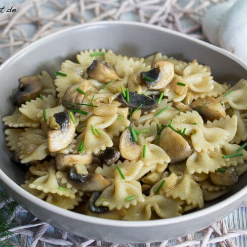Schüssel mit Farfalle-Nudeln Nudelsalat mit Pilzen und Schnittlauch.