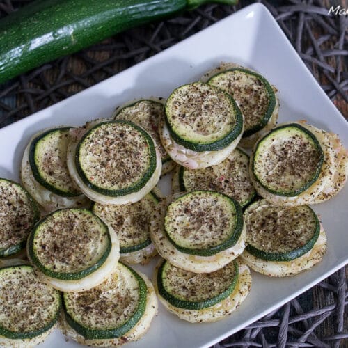Blätterteig mit Zucchini Fingerfood 3 In Scheiben geschnittene und gewürzter Blätterteig mit Zucchini sind auf einem weißen Teller gestapelt.