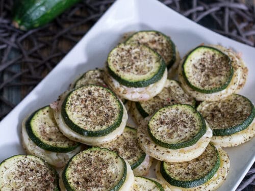 Mit Kräutern gewürzte, in Scheiben geschnittene Zucchini auf Blätterteig auf einem weißen Teller, mit ganzen Zucchini im Hintergrund.