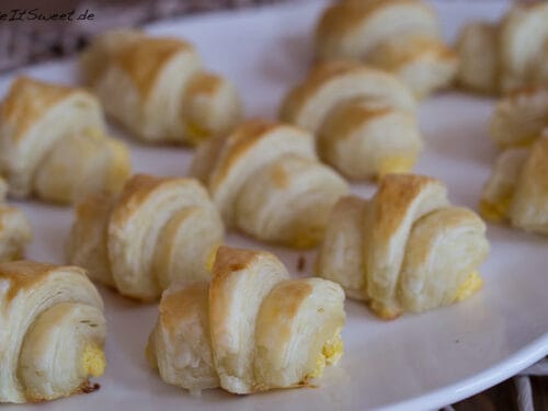 Mini-Blätterteig-Croissants und mit Kürbis gefüllte als Fingerfood auf einem weißen Teller.