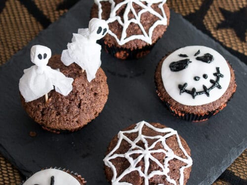 Sechs Halloween-Cupcakes auf einem schwarzen Tablett mit unterschiedlicher Dekoration.
