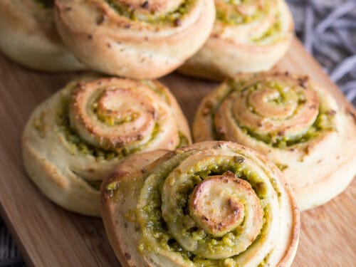 Sechs Mini Hefeschnecken mit grüner Pistazienfüllung, dicht aneinander gereiht auf einem Holzbrett.