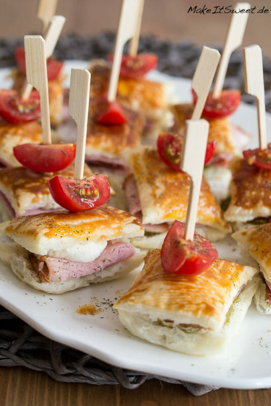 Mini Blätterteig Sandwiches gefüllt mit Schinken und Mozzarella an einem Spieß mit einer Tomate