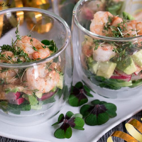 Garnelen Cocktail Salat im Glas 3 Glasschalen mit Garnelen-Salat mit Radieschen, Avocado und Feldsalat, garniert mit Kresse auf einem weißen Teller.