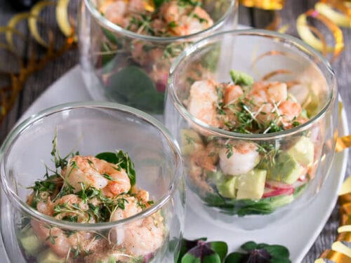 Drei Glasschalen gefüllt mit Garnelen-Cocktail-Salat mit Feldsalat, Radieschen und Avocado, garniert mit Kresse, angerichtet auf einem weißen Tablett.